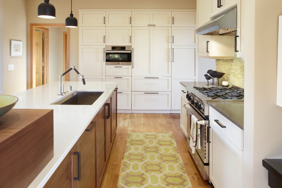 他の地域にある広いコンテンポラリースタイルのおしゃれなキッチン (アンダーカウンターシンク、シェーカースタイル扉のキャビネット、白いキャビネット、クオーツストーンカウンター、緑のキッチンパネル、ガラス板のキッチンパネル、シルバーの調理設備、無垢フローリング、茶色い床、白いキッチンカウンター) の写真
