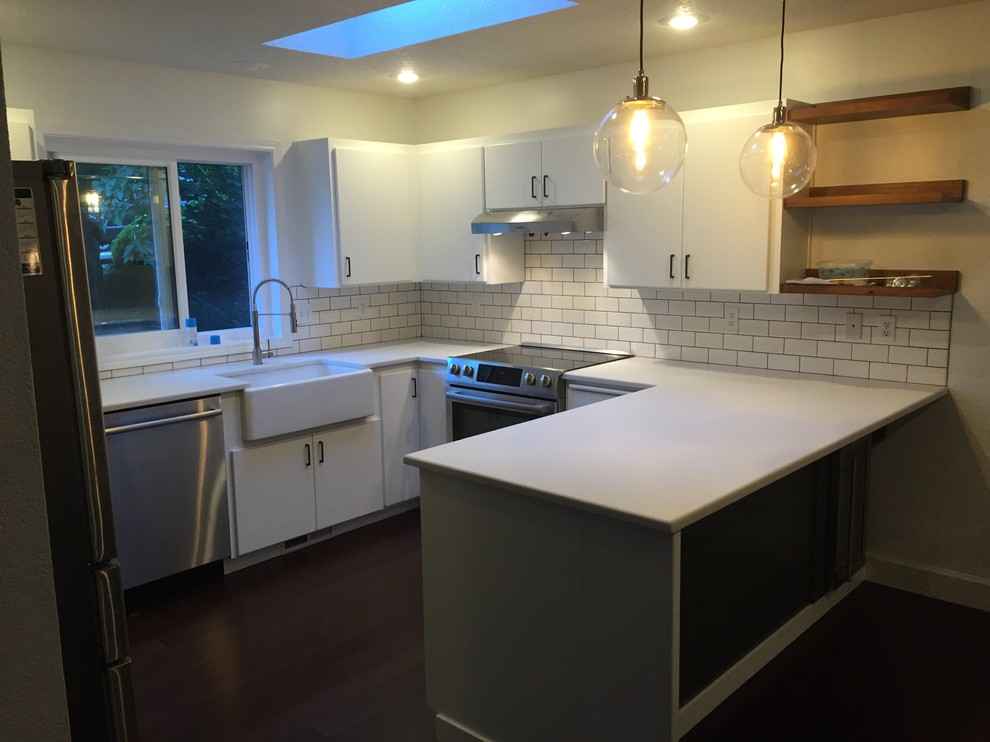 Small trendy u-shaped eat-in kitchen photo in Portland with a farmhouse sink, flat-panel cabinets, white cabinets, solid surface countertops, white backsplash, subway tile backsplash, stainless steel appliances and a peninsula