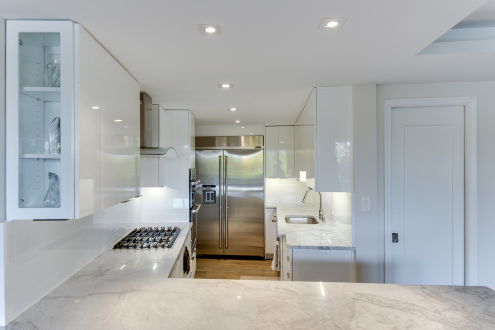 Esempio di una cucina design di medie dimensioni con lavello sottopiano, ante bianche, top in granito, paraspruzzi bianco, elettrodomestici in acciaio inossidabile e penisola