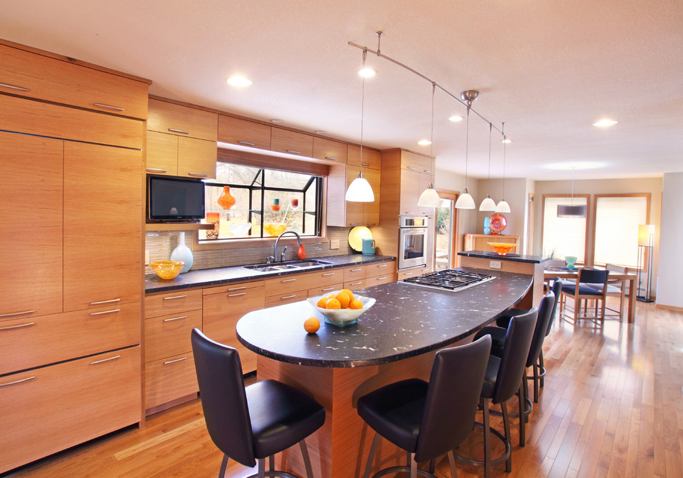 This is an example of a medium sized contemporary galley kitchen/diner in Minneapolis with a triple-bowl sink, flat-panel cabinets, light wood cabinets, granite worktops, grey splashback, stainless steel appliances, light hardwood flooring and an island.