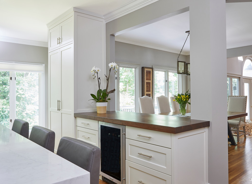Inredning av ett modernt stort vit vitt kök och matrum, med en undermonterad diskho, skåp i shakerstil, vita skåp, marmorbänkskiva, vitt stänkskydd, stänkskydd i keramik, rostfria vitvaror, mellanmörkt trägolv och en köksö