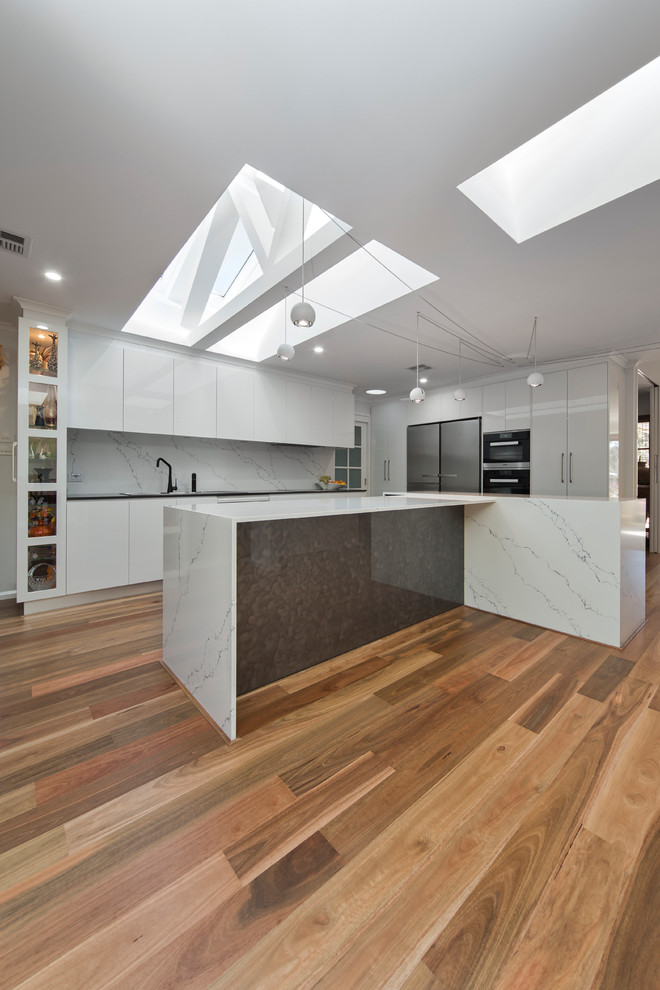 This is an example of a modern kitchen in Canberra - Queanbeyan with a built-in sink, white cabinets, quartz worktops, white splashback, stone slab splashback, stainless steel appliances, medium hardwood flooring and multiple islands.