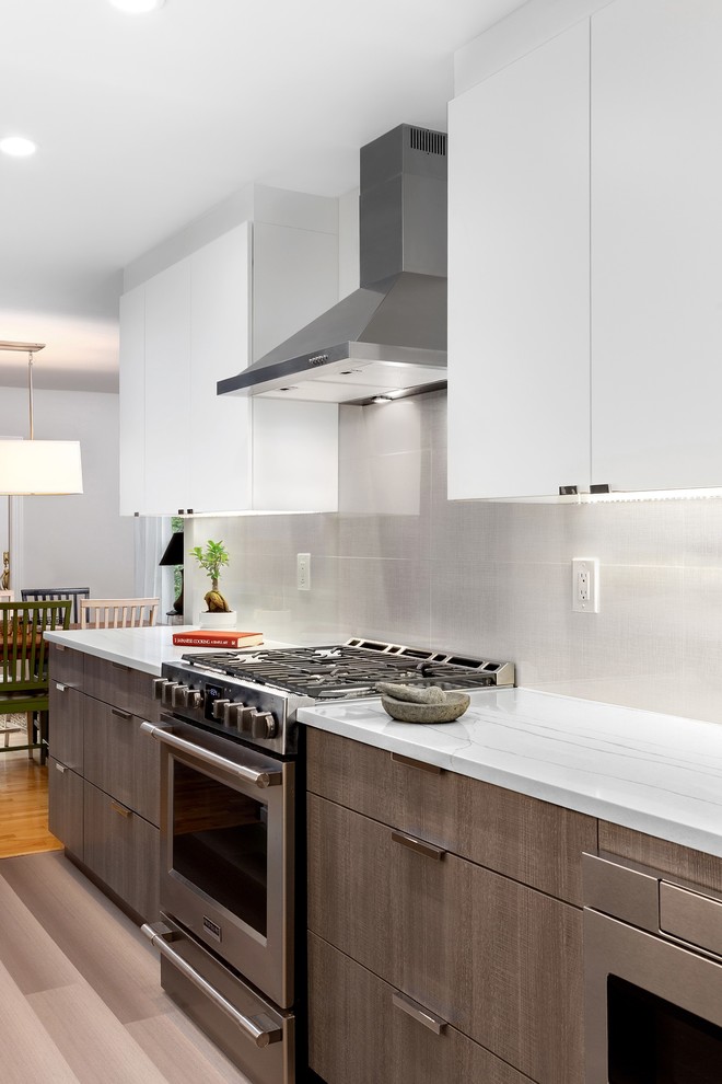 Inredning av ett modernt mellanstort vit vitt kök, med en undermonterad diskho, släta luckor, vita skåp, bänkskiva i kvarts, grått stänkskydd, stänkskydd i porslinskakel, rostfria vitvaror, laminatgolv och grått golv