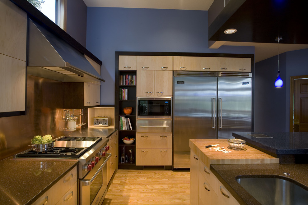 Foto på ett funkis kök, med rostfria vitvaror, bänkskiva i kvarts, en undermonterad diskho, släta luckor, skåp i ljust trä, stänkskydd med metallisk yta och stänkskydd i metallkakel