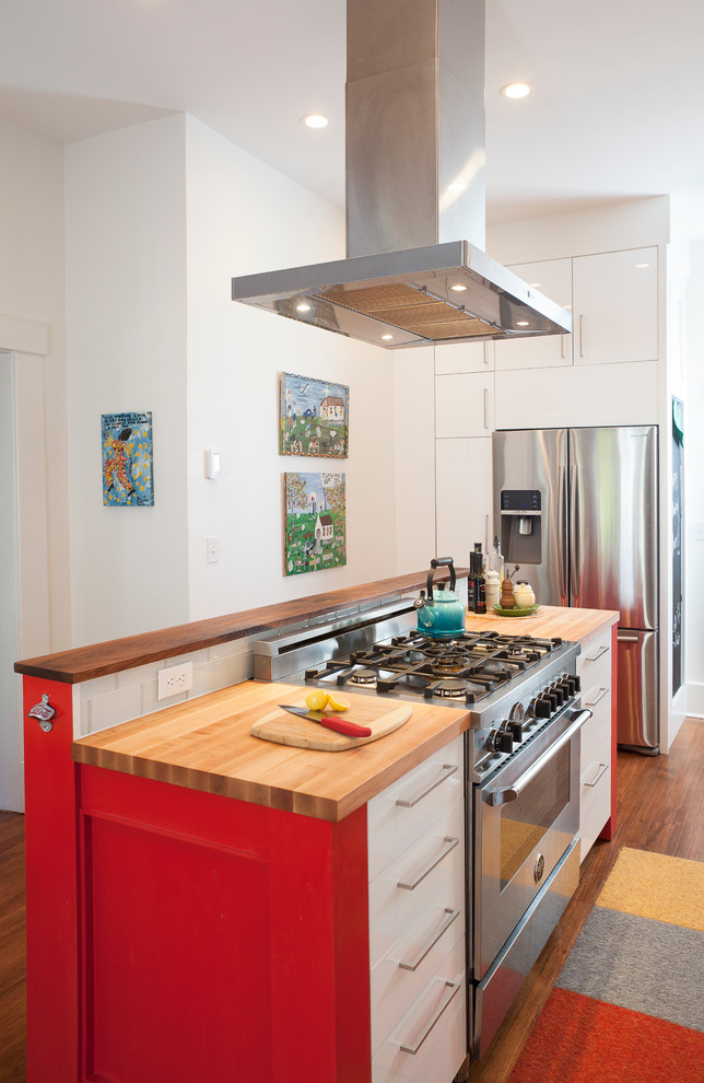 Moderne Küche mit flächenbündigen Schrankfronten, roten Schränken, Arbeitsplatte aus Holz, Küchenrückwand in Weiß, Rückwand aus Metrofliesen und Küchengeräten aus Edelstahl in Sonstige