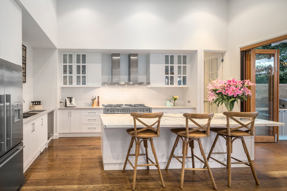 Mid-sized trendy l-shaped medium tone wood floor eat-in kitchen photo in Melbourne with an undermount sink, recessed-panel cabinets, white cabinets, marble countertops, stainless steel appliances and an island