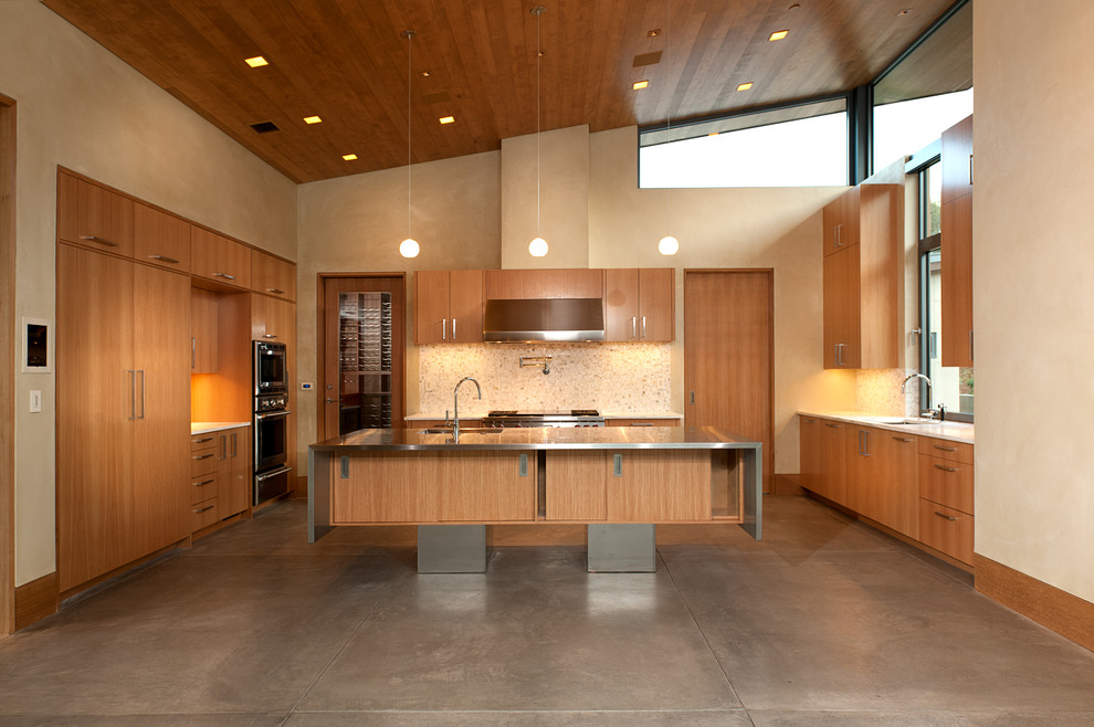 Moderne Küche in U-Form mit flächenbündigen Schrankfronten, hellbraunen Holzschränken, Edelstahl-Arbeitsplatte, Küchenrückwand in Beige, Küchengeräten aus Edelstahl, Betonboden und Kücheninsel in San Luis Obispo