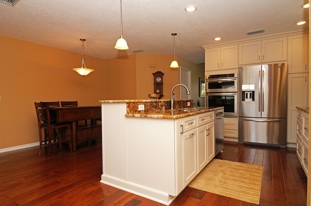 Example of a mid-sized trendy eat-in kitchen design in Tampa with a double-bowl sink, beige cabinets, granite countertops, beige backsplash, stone tile backsplash, stainless steel appliances and an island