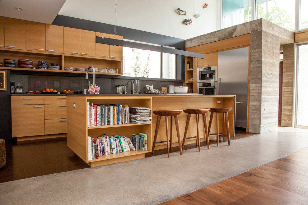 Cette image montre une cuisine design en bois clair avec un placard à porte plane, une crédence grise et un électroménager en acier inoxydable.