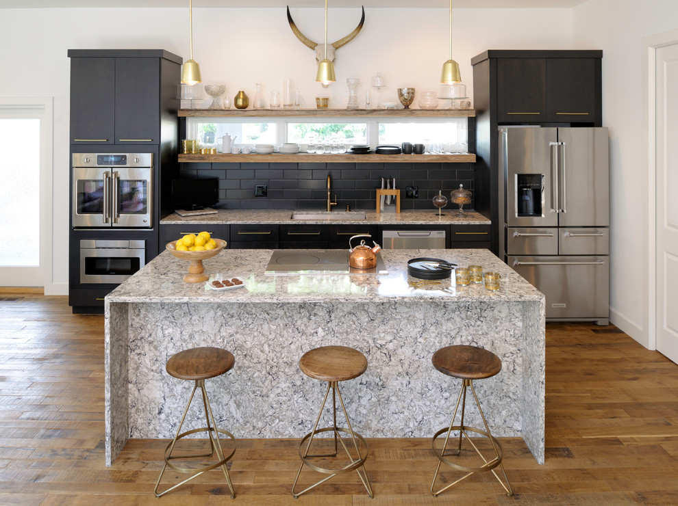 Example of a trendy single-wall medium tone wood floor open concept kitchen design in St Louis with an undermount sink, flat-panel cabinets, black cabinets, black backsplash, subway tile backsplash, stainless steel appliances, an island, granite countertops and gray countertops