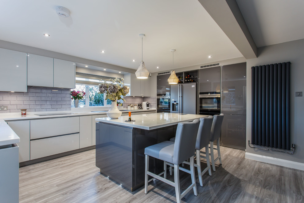 Contemporary u-shaped kitchen in Sussex with a built-in sink, flat-panel cabinets, grey cabinets, grey splashback, metro tiled splashback, integrated appliances, an island and grey floors.
