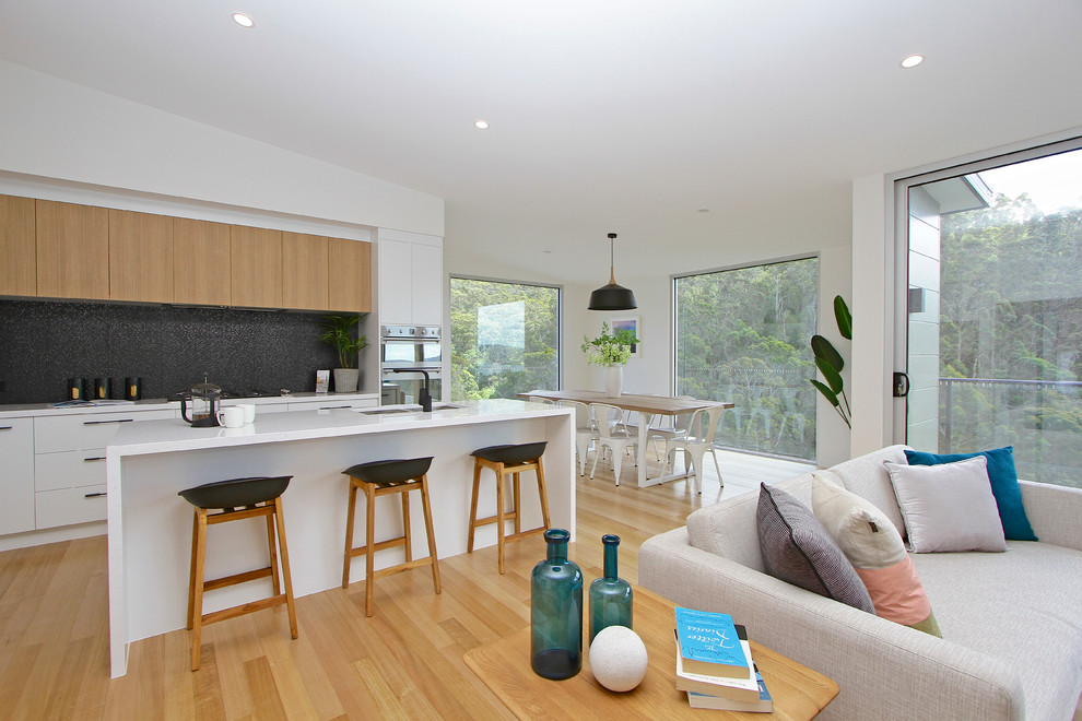 Zweizeilige Moderne Küche mit flächenbündigen Schrankfronten, hellbraunen Holzschränken, Küchenrückwand in Schwarz, braunem Holzboden und Kücheninsel in Hobart