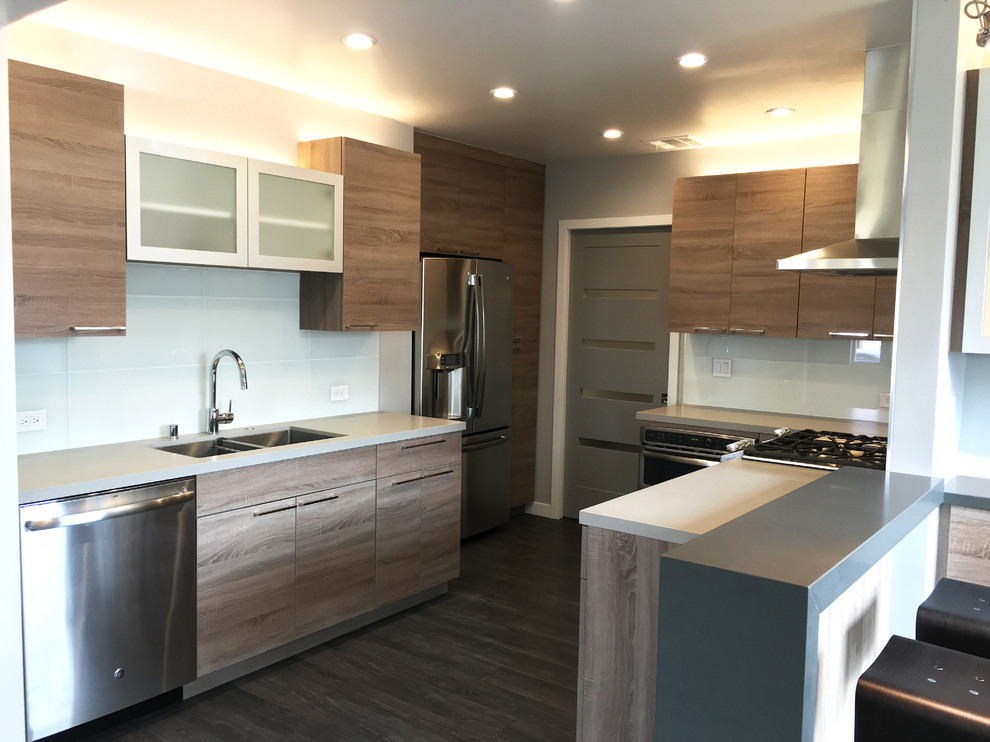 Example of a mid-sized trendy eat-in kitchen design in Los Angeles with an undermount sink, glass-front cabinets, light wood cabinets, solid surface countertops, white backsplash, glass tile backsplash, stainless steel appliances and a peninsula