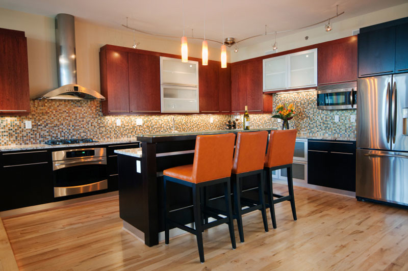 Bild på ett mellanstort funkis kök, med släta luckor, röda skåp, flerfärgad stänkskydd, stänkskydd i mosaik, rostfria vitvaror, ljust trägolv och en köksö