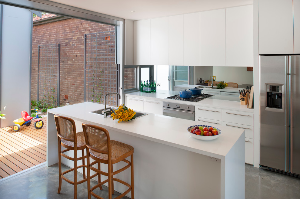 Свежая идея для дизайна: параллельная кухня-гостиная в современном стиле с накладной мойкой, плоскими фасадами, белыми фасадами, зеркальным фартуком, техникой из нержавеющей стали, бетонным полом и островом - отличное фото интерьера