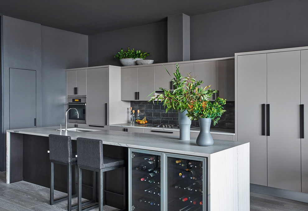 Cette photo montre une cuisine parallèle tendance avec un évier encastré, un placard à porte plane, des portes de placard grises, une crédence grise, un électroménager en acier inoxydable, îlot et un sol gris.