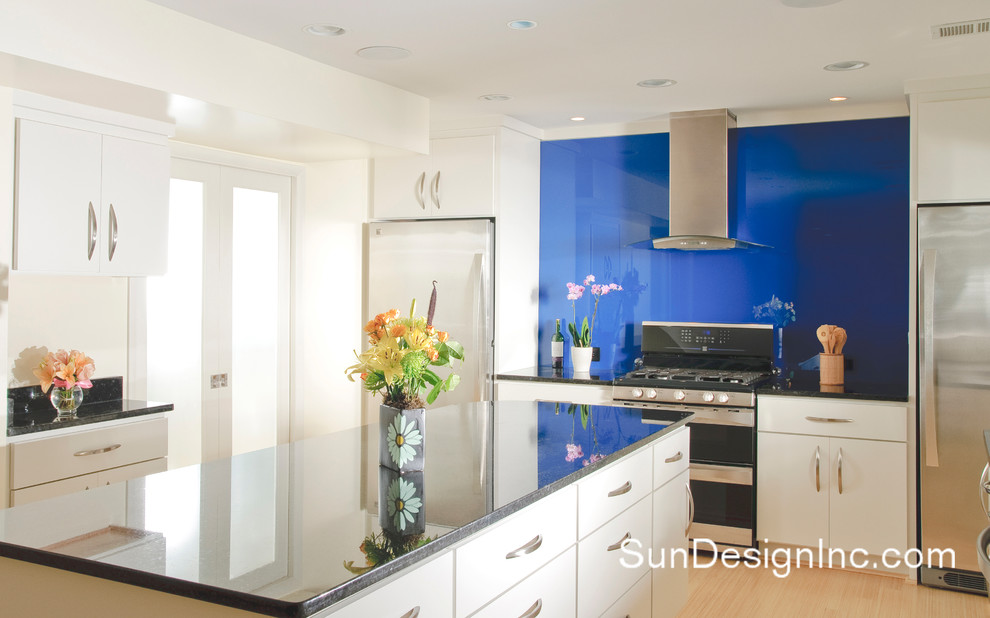 Foto di una cucina design con lavello sottopiano, ante lisce, ante bianche, top in vetro, paraspruzzi blu, elettrodomestici in acciaio inossidabile e pavimento in bambù