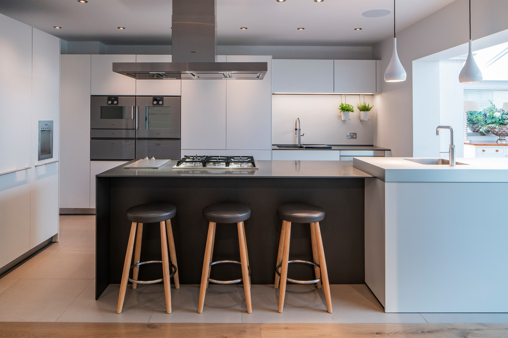 Design ideas for a large contemporary l-shaped kitchen in Surrey with flat-panel cabinets, stainless steel appliances, an island, white floors and black worktops.