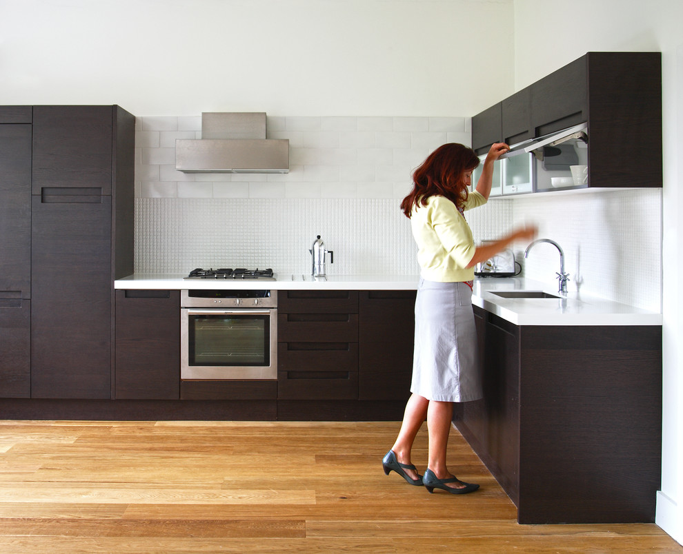 Источник вдохновения для домашнего уюта: кухня в современном стиле с врезной мойкой, плоскими фасадами, темными деревянными фасадами и белым фартуком