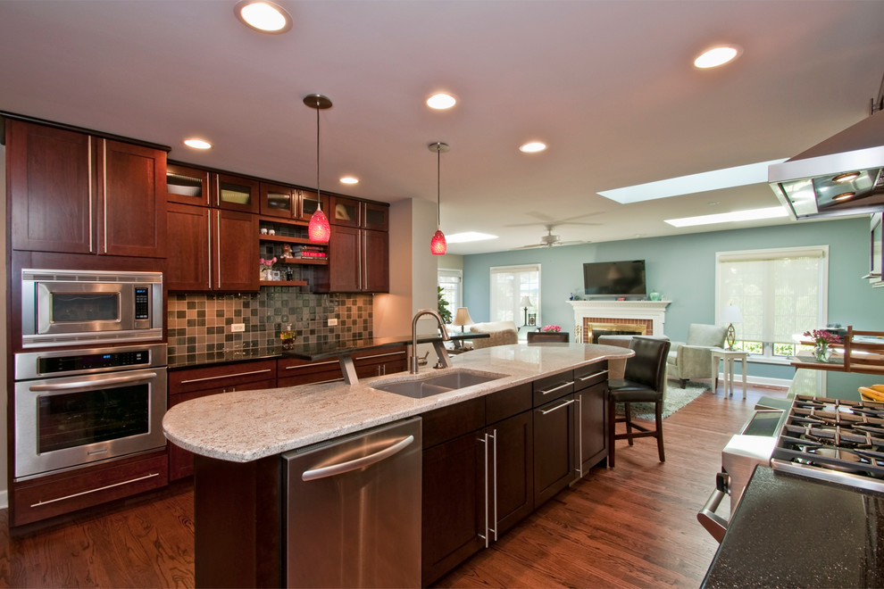 Example of a trendy galley medium tone wood floor and brown floor eat-in kitchen design in Chicago with an undermount sink, recessed-panel cabinets, dark wood cabinets, granite countertops, gray backsplash, glass tile backsplash and stainless steel appliances