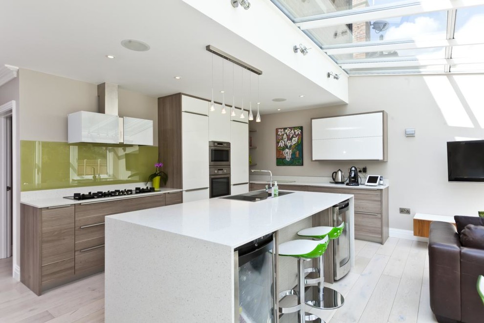 Moderne Küche mit flächenbündigen Schrankfronten, hellbraunen Holzschränken, Küchenrückwand in Grün, Küchengeräten aus Edelstahl, gebeiztem Holzboden und Kücheninsel in Surrey