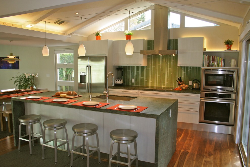 Immagine di una cucina minimalista di medie dimensioni con elettrodomestici in acciaio inossidabile, lavello sottopiano, ante lisce, ante grigie, top in granito, paraspruzzi verde, paraspruzzi con piastrelle di vetro e pavimento in legno massello medio