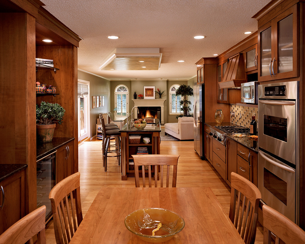 Example of a transitional galley light wood floor eat-in kitchen design in Bridgeport with glass-front cabinets, multicolored backsplash, stainless steel appliances, a double-bowl sink, medium tone wood cabinets, granite countertops and an island