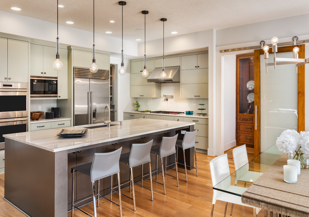 Contemporary l-shaped kitchen/diner in San Diego with a submerged sink, flat-panel cabinets, green cabinets, white splashback, stainless steel appliances, medium hardwood flooring and an island.