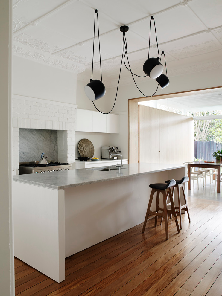 Imagen de cocina comedor actual de tamaño medio con una isla, fregadero bajoencimera, electrodomésticos de acero inoxidable y suelo de madera en tonos medios