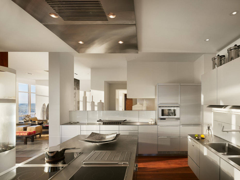 Exempel på ett modernt kök, med en integrerad diskho, släta luckor, vita skåp, bänkskiva i rostfritt stål, vitt stänkskydd, mörkt trägolv och en köksö