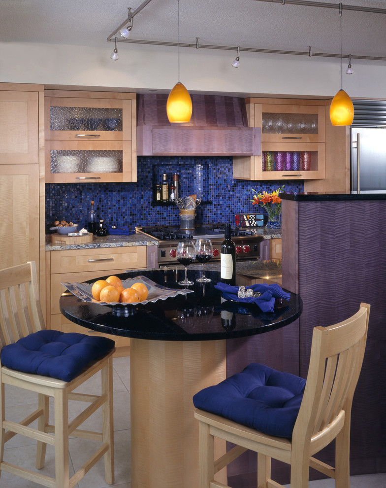 Réalisation d'une cuisine design en bois clair avec un placard avec porte à panneau encastré, une crédence bleue et une crédence en carreau de verre.