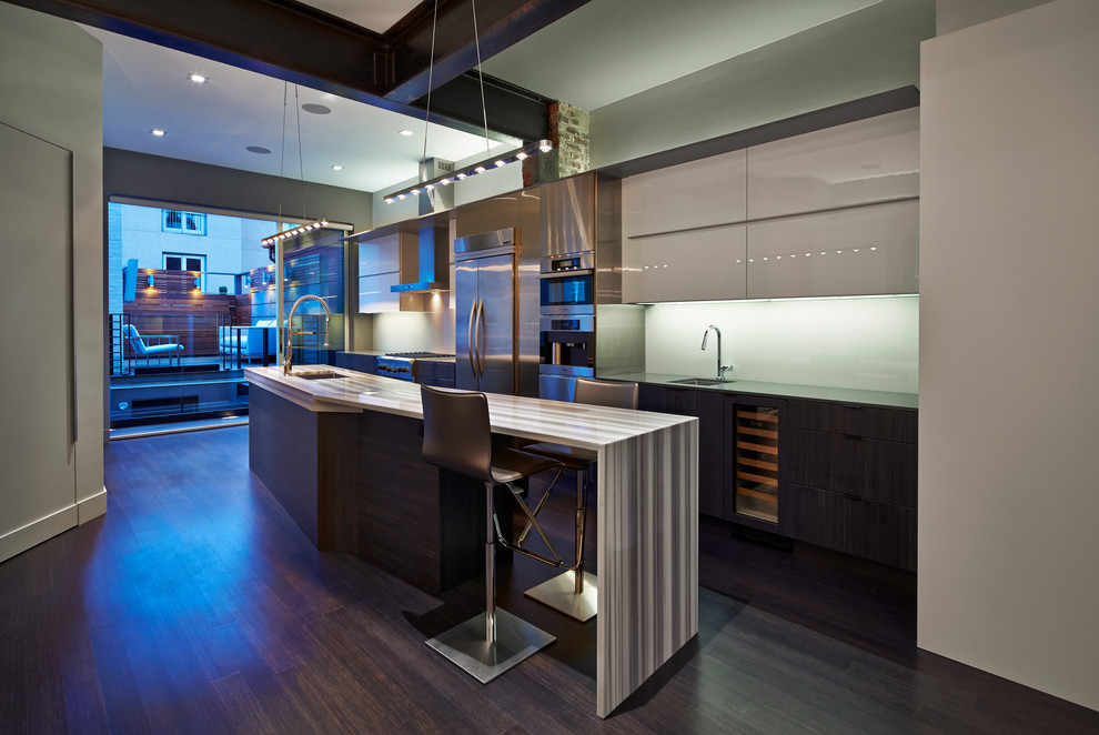 Moderne Küche mit Unterbauwaschbecken, flächenbündigen Schrankfronten, grauen Schränken, Küchenrückwand in Weiß, Glasrückwand, Küchengeräten aus Edelstahl, dunklem Holzboden und Kücheninsel in Los Angeles