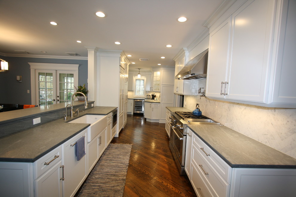 Inspiration for a large contemporary l-shaped medium tone wood floor kitchen remodel in New York with a farmhouse sink, recessed-panel cabinets, white cabinets, soapstone countertops, gray backsplash and marble backsplash