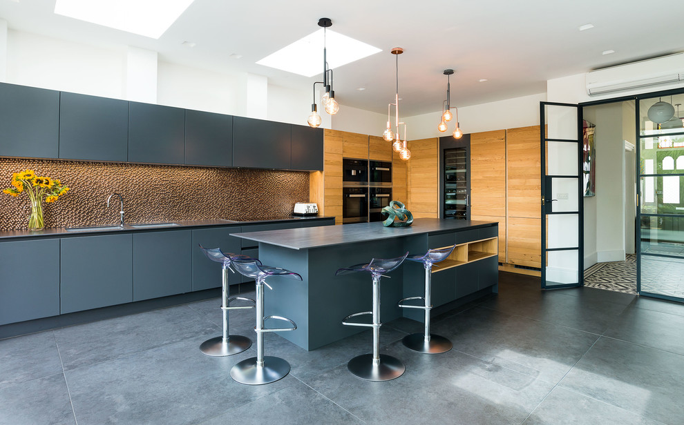 Contemporary l-shaped kitchen in London with a double-bowl sink, flat-panel cabinets, blue cabinets, metallic splashback, an island, grey floors and grey worktops.