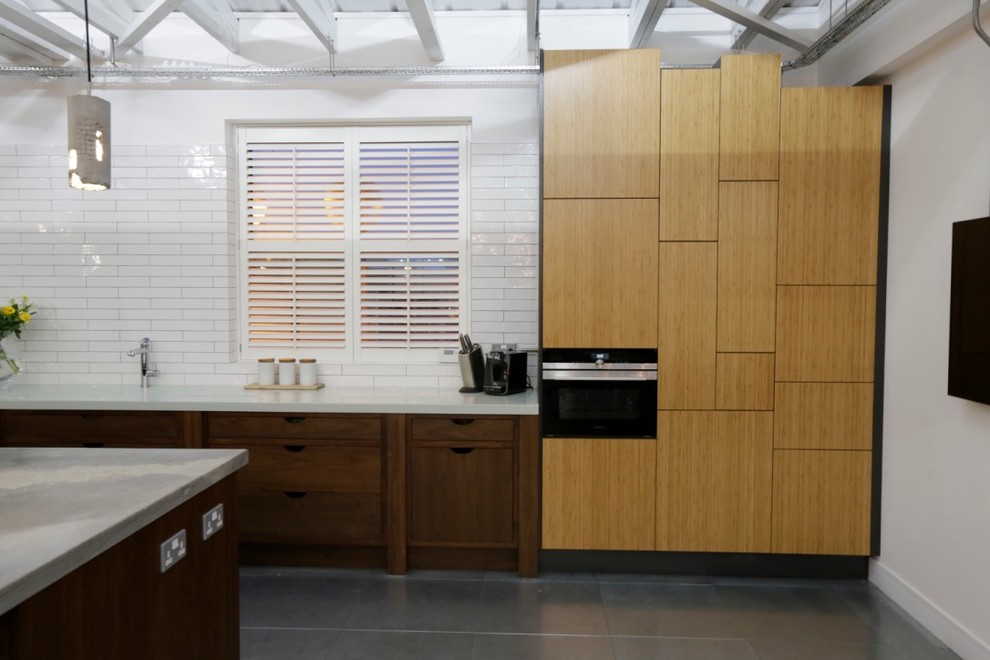На фото: большая прямая кухня-гостиная в современном стиле с накладной мойкой, плоскими фасадами, фасадами цвета дерева среднего тона, столешницей из бетона, черной техникой и островом