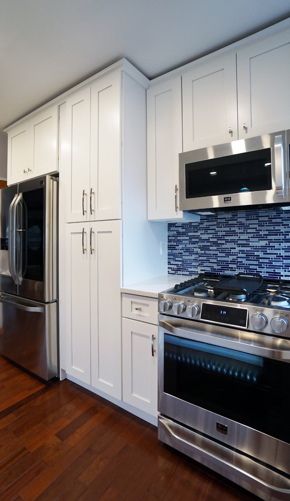 ニューヨークにある高級な広いコンテンポラリースタイルのおしゃれなキッチン (エプロンフロントシンク、シェーカースタイル扉のキャビネット、白いキャビネット、クオーツストーンカウンター、青いキッチンパネル、ガラスタイルのキッチンパネル、シルバーの調理設備、濃色無垢フローリング、茶色い床) の写真