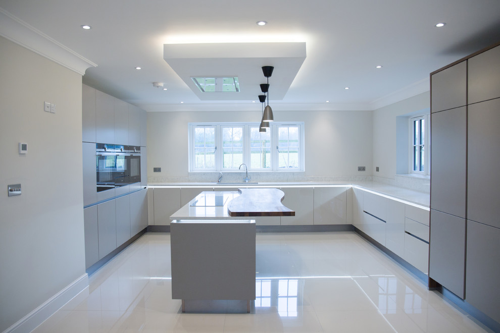 Große Moderne Wohnküche in U-Form mit Einbauwaschbecken, flächenbündigen Schrankfronten, beigen Schränken, Quarzit-Arbeitsplatte, schwarzen Elektrogeräten, Porzellan-Bodenfliesen und Kücheninsel in Buckinghamshire