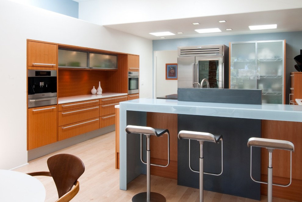 Eat-in kitchen - large contemporary u-shaped light wood floor and beige floor eat-in kitchen idea in San Diego with an undermount sink, flat-panel cabinets, medium tone wood cabinets, glass countertops, stainless steel appliances, an island, brown backsplash, wood backsplash and white countertops