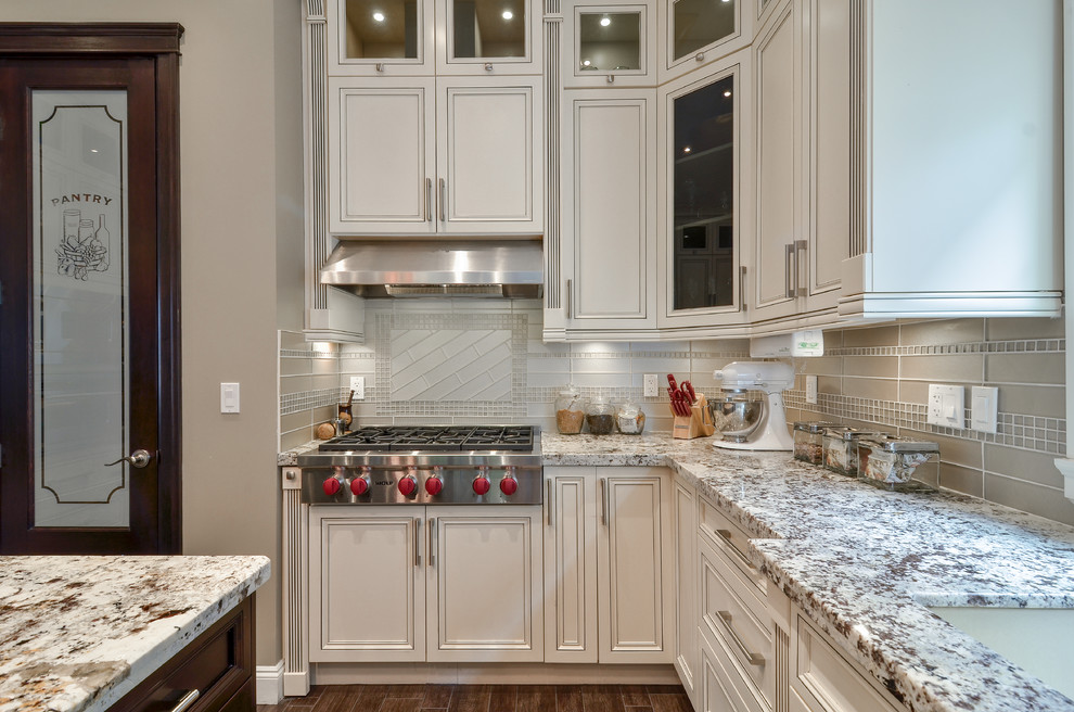 Example of a large trendy l-shaped light wood floor eat-in kitchen design in Vancouver with recessed-panel cabinets, an island, an undermount sink, white cabinets, granite countertops, glass tile backsplash, stainless steel appliances and beige backsplash