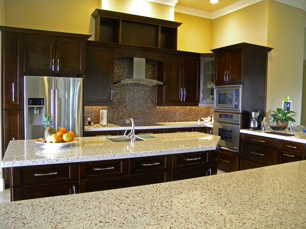 Modern inredning av ett stort kök, med en undermonterad diskho, luckor med infälld panel, skåp i mörkt trä, bänkskiva i återvunnet glas, brunt stänkskydd, stänkskydd i mosaik, rostfria vitvaror och en köksö