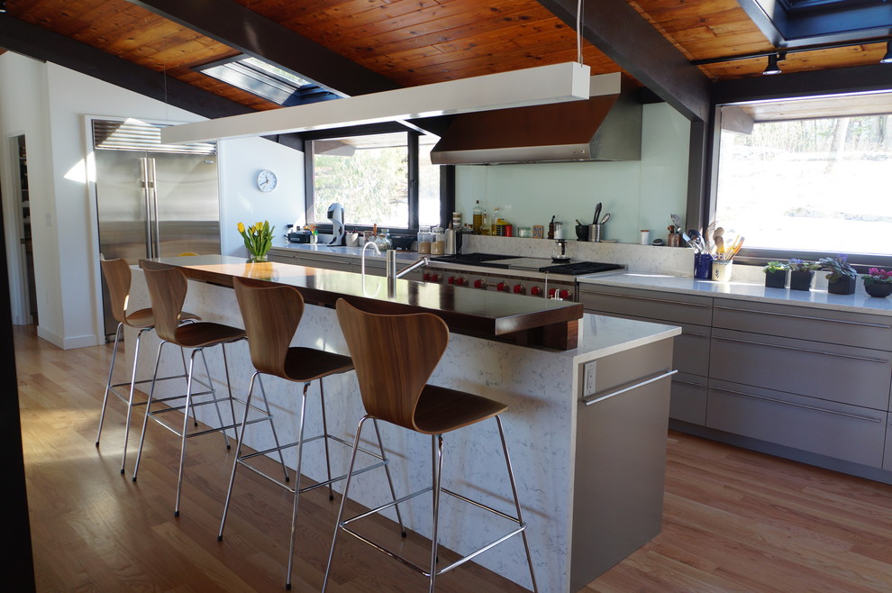 Idéer för att renovera ett mellanstort funkis grå grått kök, med släta luckor, grå skåp, träbänkskiva, grönt stänkskydd, stänkskydd i glaskakel, rostfria vitvaror, ljust trägolv, en köksö, en enkel diskho och brunt golv