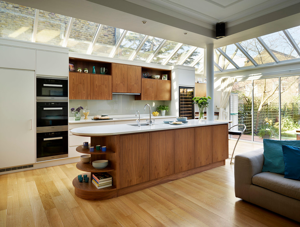 Cette image montre une très grande cuisine ouverte design avec un placard à porte plane, un plan de travail en surface solide, une crédence en feuille de verre, îlot et une crédence grise.