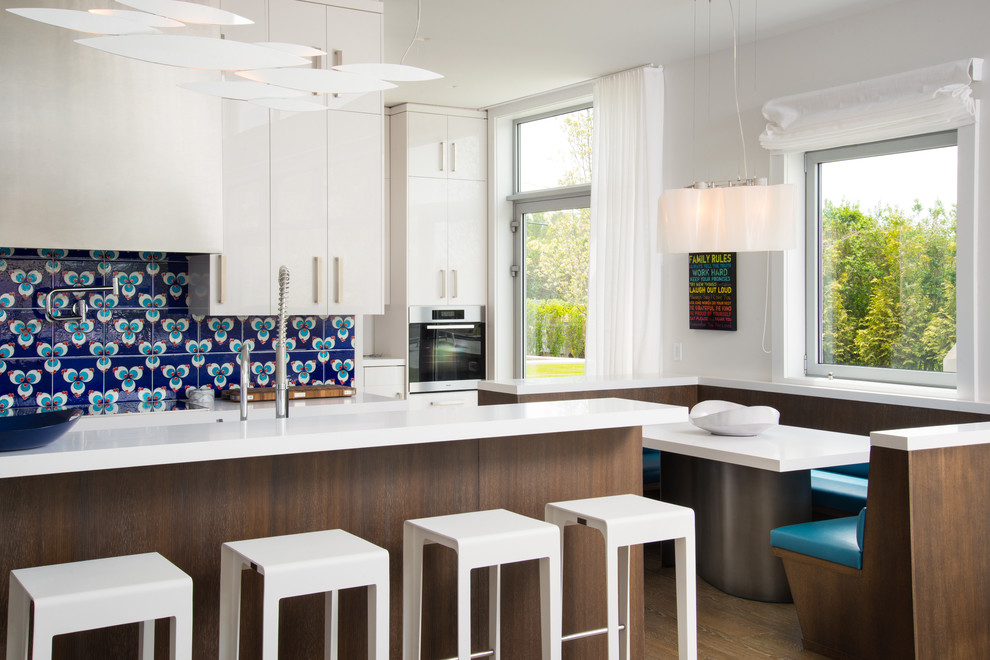 На фото: параллельная кухня среднего размера в современном стиле с обеденным столом, плоскими фасадами, белыми фасадами, синим фартуком и островом
