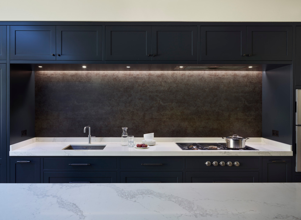 This is an example of a large contemporary l-shaped kitchen/diner in London with an integrated sink, recessed-panel cabinets, grey cabinets, quartz worktops, grey splashback, stone slab splashback, stainless steel appliances, medium hardwood flooring, an island, brown floors and white worktops.
