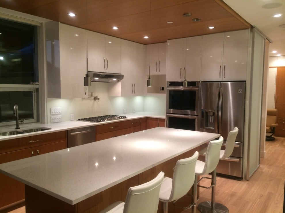 Foto di una cucina abitabile contemporanea con lavello sottopiano, ante lisce, ante bianche, top in superficie solida e elettrodomestici in acciaio inossidabile