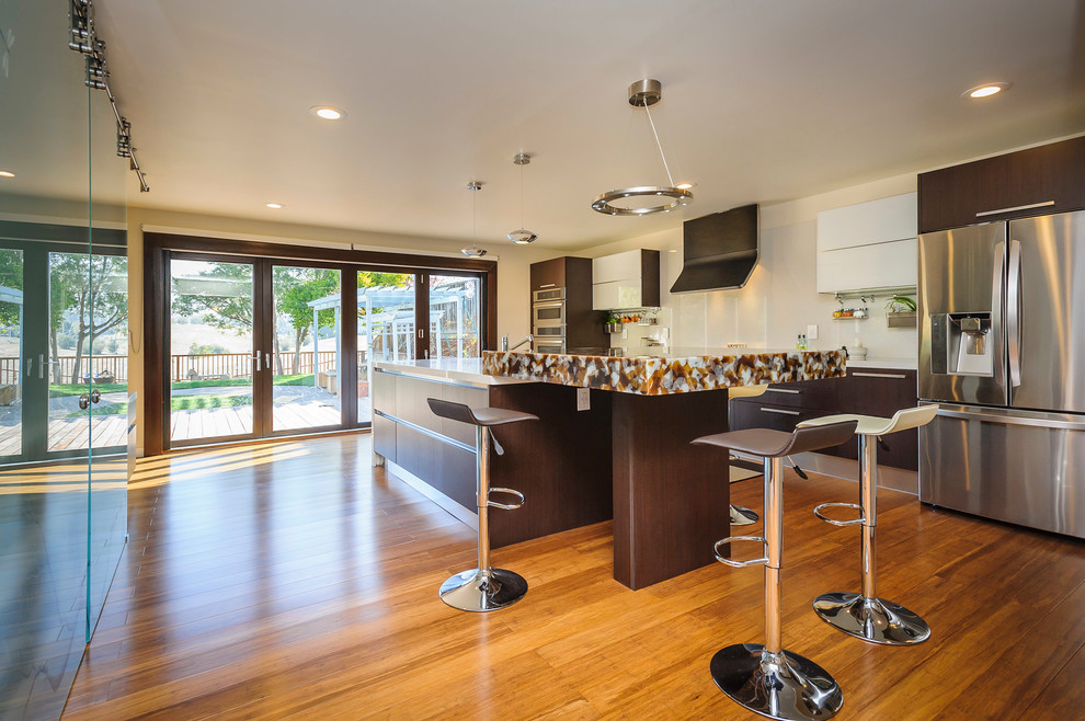 Photo of a contemporary u-shaped kitchen/diner in San Francisco with a submerged sink, brown cabinets, engineered stone countertops, white splashback, stone slab splashback and stainless steel appliances.