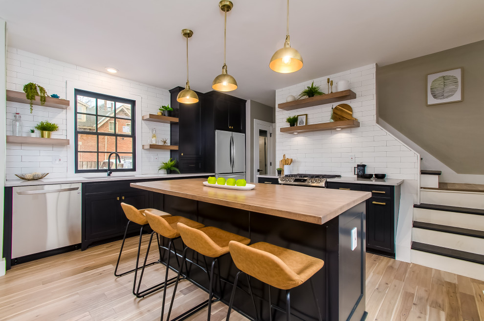 Medium sized contemporary l-shaped kitchen/diner in Columbus with a belfast sink, recessed-panel cabinets, engineered stone countertops, white splashback, ceramic splashback, black appliances, light hardwood flooring, an island, black floors, multicoloured worktops and a timber clad ceiling.