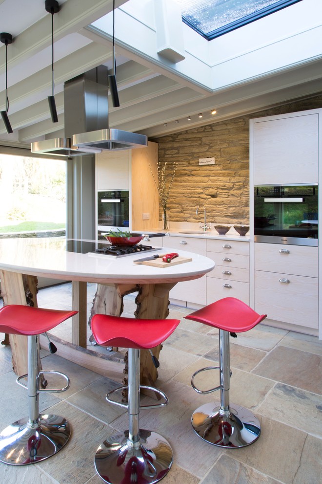Photo of a small modern single-wall kitchen/diner in Cornwall with a single-bowl sink, flat-panel cabinets, light wood cabinets, engineered stone countertops, stainless steel appliances and an island.