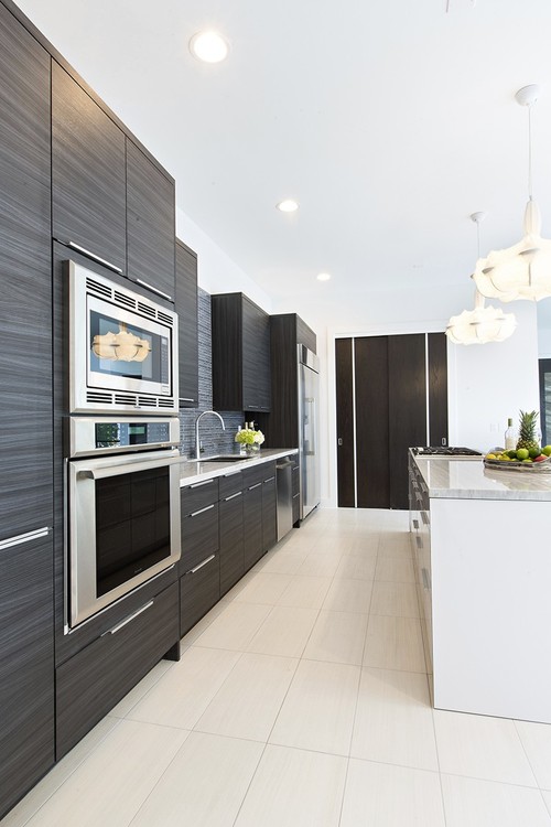 Modern galley kitchen with dark wood-grain laminate flat-panel cabinets, integrated stainless appliances, and a white island under pendant lights