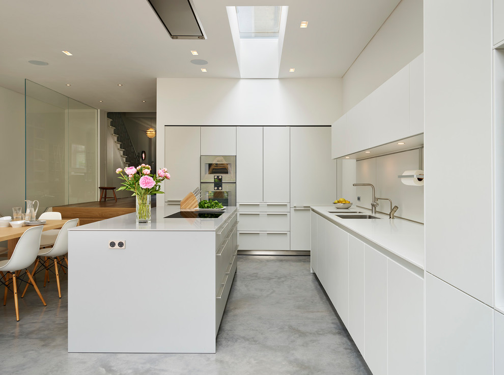 Свежая идея для дизайна: угловая кухня среднего размера в современном стиле с двойной мойкой, плоскими фасадами, белыми фасадами, белым фартуком, бетонным полом, островом, серым полом и обеденным столом - отличное фото интерьера